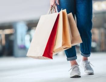 A person wearing sneakers and cuffed jeans carries shopping bags through a mall