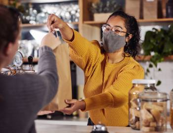 A woman working a cash register passes a customer their bag