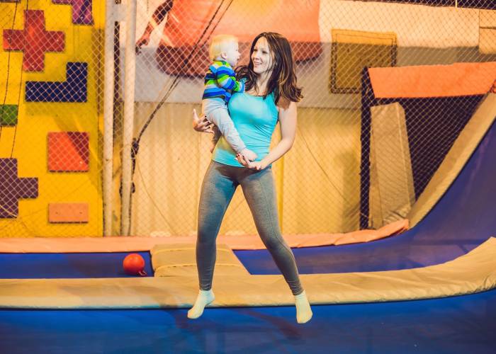 A mom and young child jump on an indoor trampoline place