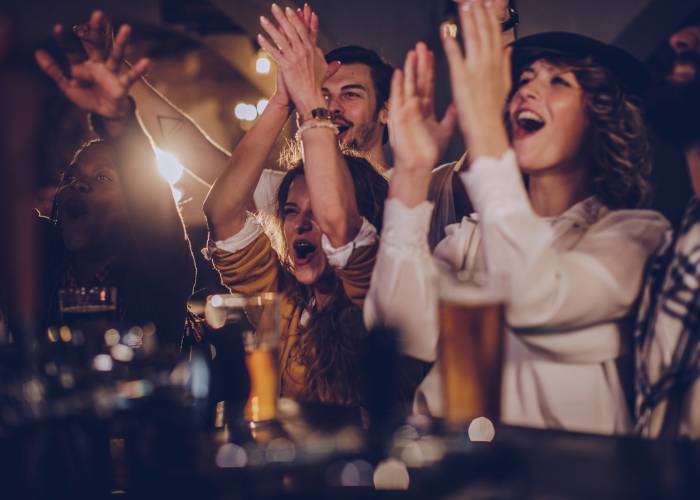 A crowd cheers at a show while drinking beverages